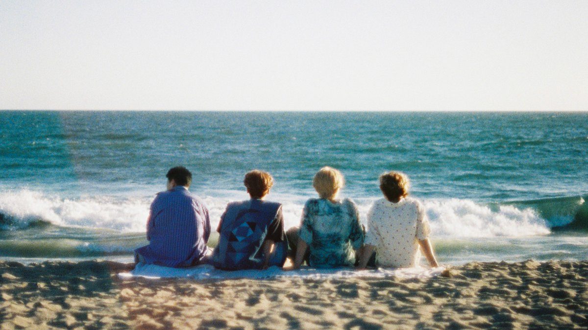 生FIRST新CMのワンシーン、海辺に座る4人の後ろ姿