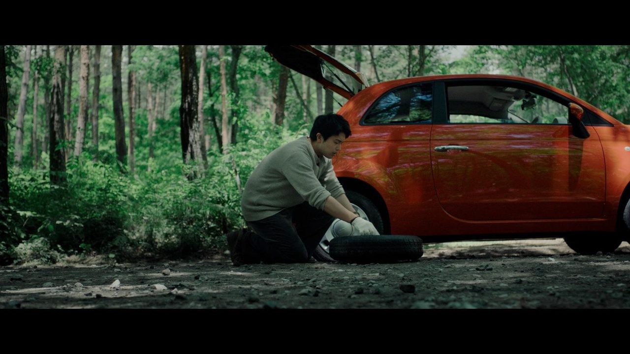 オレンジ色の車のタイヤ交換をするシーン