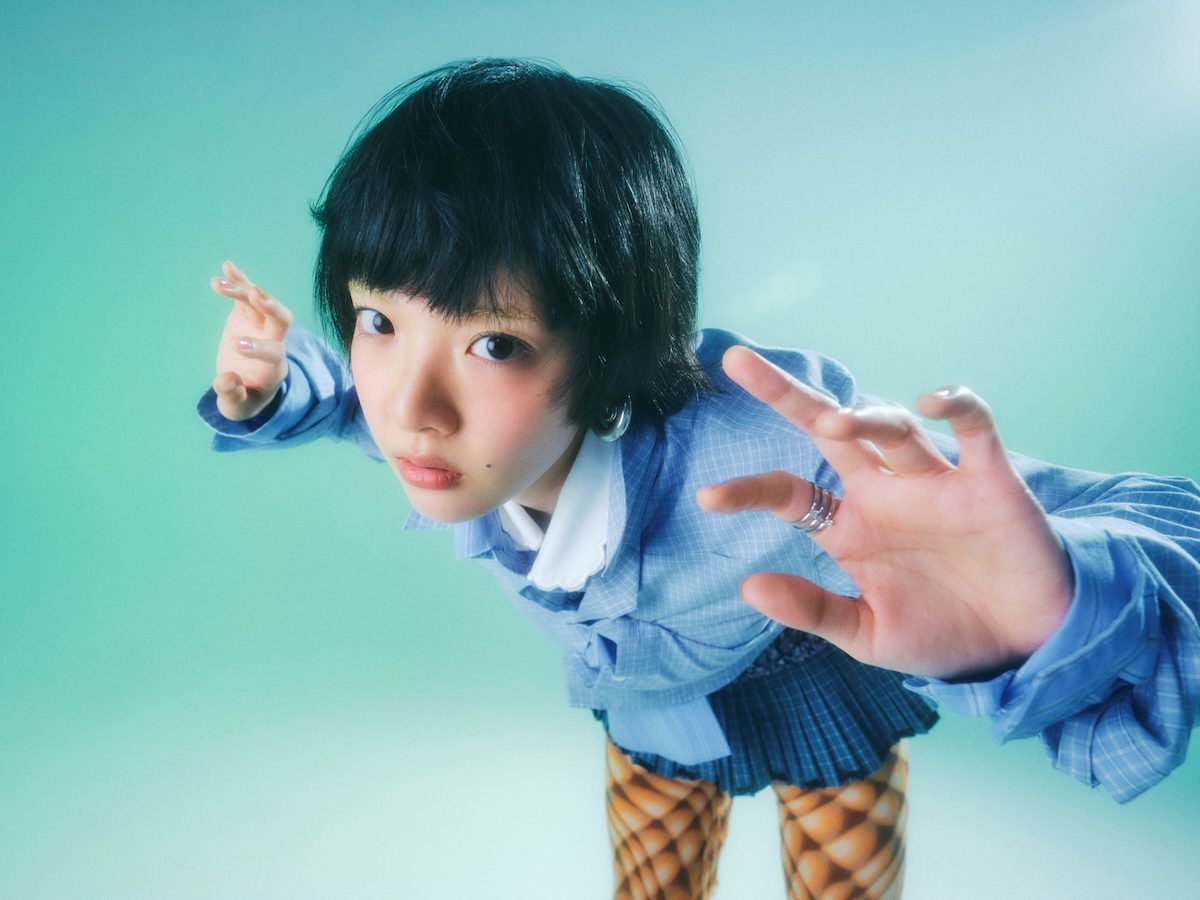青緑の背景でカメラに手を伸ばすあいみょんのアーティスト写真