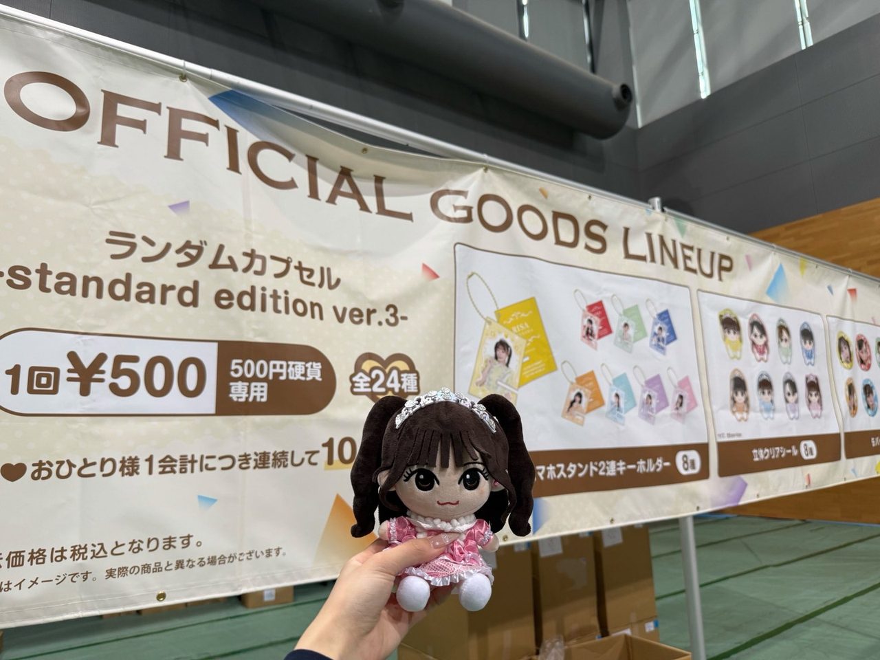 会場のグッズ売り場にあるOFFICIAL GOODS LINEUPの看板。ランダムカプセルstandard edition ver.3が1回500円と案内されている