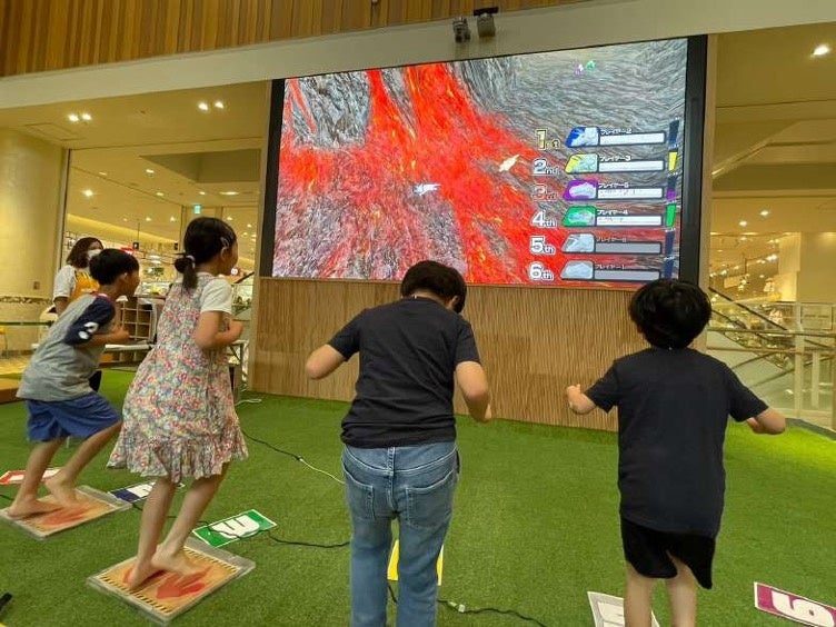 ディノグランプリ 大画面の恐竜レースで子どもたちがフットパネルを踏む様子