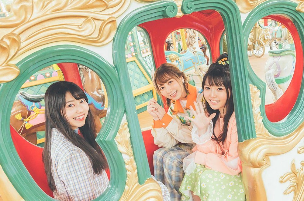 TrySailのアーティスト写真。メリーゴーラウンドの馬車の窓から顔をのぞかせる3人