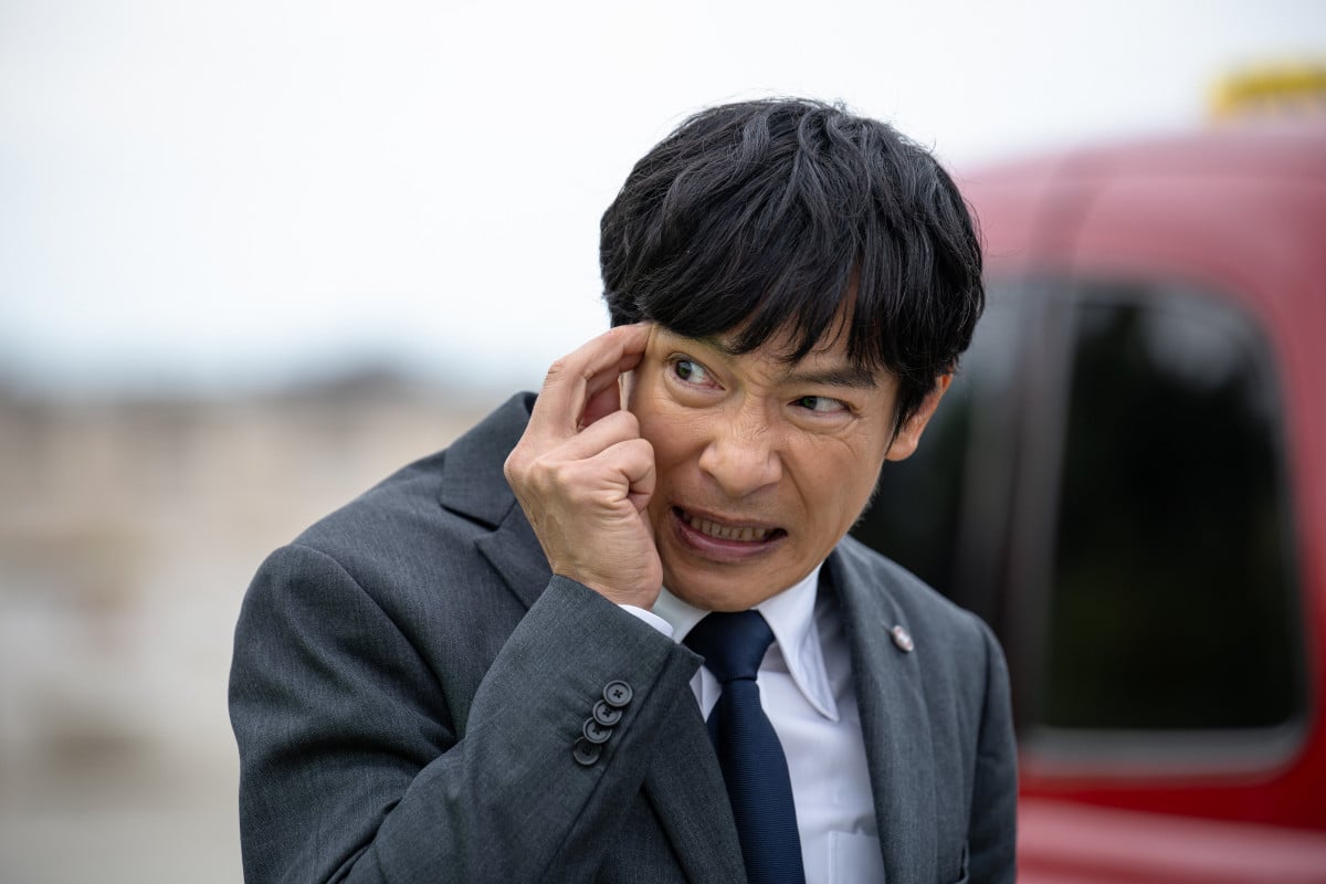 VIVANT第2シリーズ 屋外で顔に手を当てて表情を歪めるスーツ姿の男性